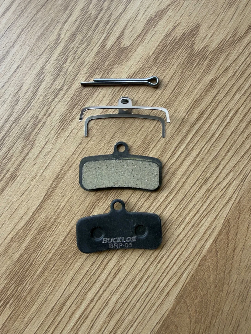 Спирачни накладки BUCKLOS BRP-05 — Накладки, пружина и шплент; една накладка показва гърба BUCKLOS BRP-05